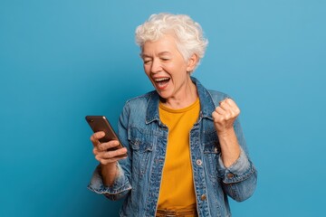 Fototapeta premium Yes, Older Woman. Caucasian Senior Female in 60s Expressing Joy and Excitement While Reading Good News on Cellphone