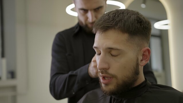 Professional barber cutting client's hair in barbershop. Clip