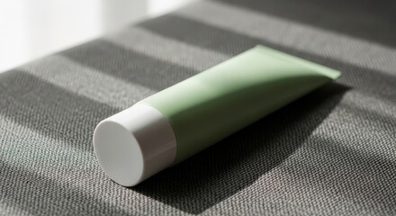 Bright sunny day light green cosmetic tube on textured gray surface with window shadow.