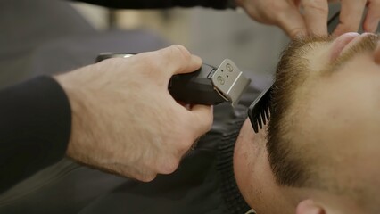 Professional barber trimming client's beard with trimmer. Clip