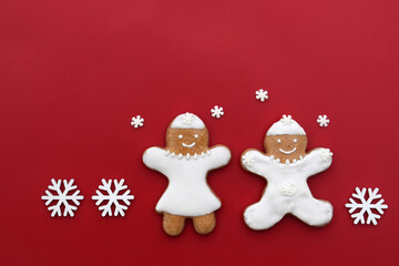 Smiling gingerbread man and woman on a red background with snowflakes around, copy space for text. Christmas time