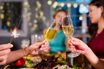 Beautiful woman having fun with group of friends clinking champagne glasses during celebration party. Drink concept.