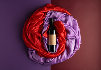 Bottle of red wine against a background of draped red and purple silk fabric.