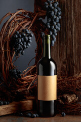 Bottle of red wine against the backdrop of an old weathered board, dried vine, and blue grapes.