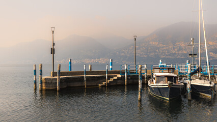 Boat is docked at a pier in front of a mountain range. Iseo in Italy