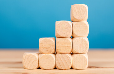 Conceptual image of wooden cubes arranged in a staircase pattern, representing growth, progress, and success. The blue background provides a cle