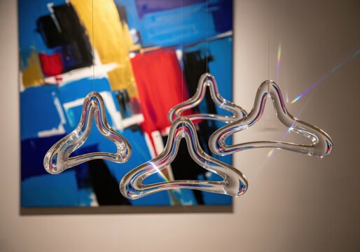 Sculptural transparent glass hangers reflecting light against a vibrant abstract painting