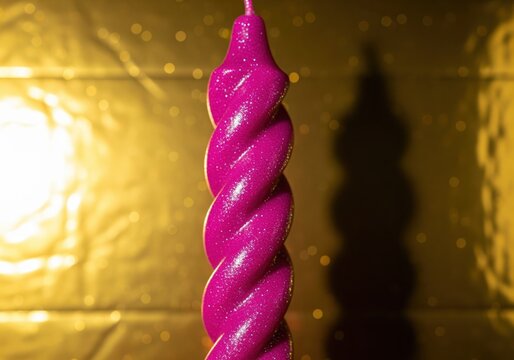 Vibrant magenta pink spiral candle with glittering texture against a golden shimmering background