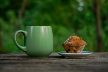 Green Ceramic Mug With Muffin On Rustic Outdoor Table In Nature Setting For Breakfast