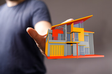 A person holding a miniature model of a modern house, representing concepts of home ownership, architecture, and design. Focus on real estate an