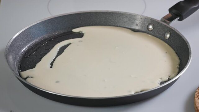 pancake batter pouring in frying pan on stovetop using ladle. close-up of cooking process for making homemade crepes in kitchen