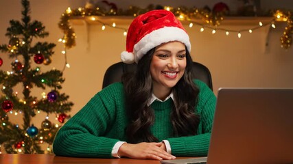 A woman in a santa hat waving and smiling during a Christmas video call, celebrating the holiday season remotely footage. - Powered by Adobe