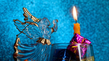 Crystal Christmas angel with trumpet beside a lit candle and shiny gifts on blue sparkle bokeh; vintage festive decor and glad tidings, winter holiday greeting background. Photo