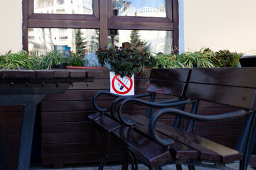 No smoking sign on table in front of building, with benches and plants around it, emphasizing importance of maintaining clean and smoke free outdoor spaces for visitors