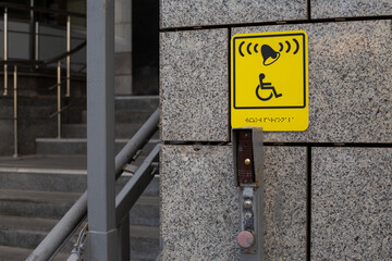 Yellow accessibility sign. Indicates call system with bell and is positioned on wall near stairs,...