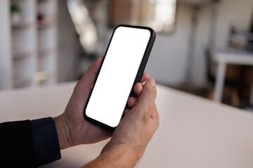 Man is holding a cell phone and looking at it. he is wearing a white shirt and black pants
