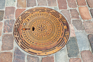 Decorative, metal sewer cover on a cobblestone street