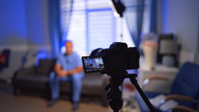 Camera records a vlog of a man sitting on the sofa talking for the video content. Selective focus on a male vlogger creating content.