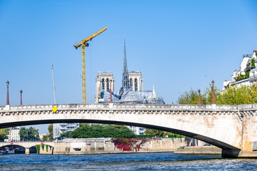 Iconic cathedral under renovation with construction crane visible, spanning a river with a bridge in the foreground, showcasing urban development