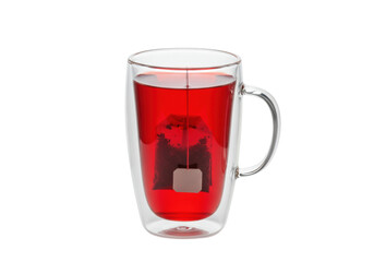 Isolated clear glass mug of red herbal tea steeped with a tea bag and handle on a table