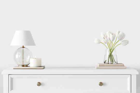 Home interior close up with dresser, glass vase with tulips, lamp and candle on empty background with free copy space. Traditional romantic room decoration. White wall mock up. 3d rendering.