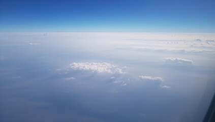 High-altitude aerial perspective through airplane window showing earth blanketed by a delicate mist and scattered clouds.