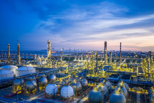 Coastal oil refinery with spherical tanks and wind turbines at dusk.