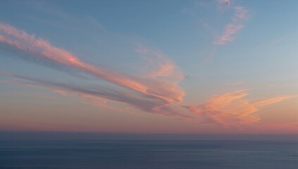 Naklejka premium Pink-hued cirrus clouds glowing above a tranquil azure sea