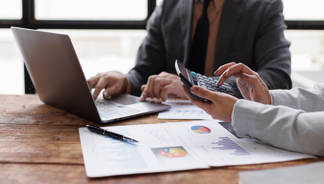 Female financial analysts with male colleague examining documents, using laptop calculator at workplace in office. Audit and taxes in business
