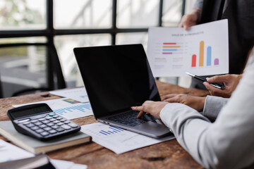 Business woman typing on laptop keyboard and financial documents, sitting at her desk in modern office, team analyzing data and preparing report
