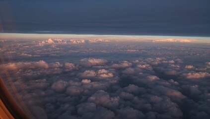 View from above of thick cumulus clouds at high elevation through an airplane window at dusk