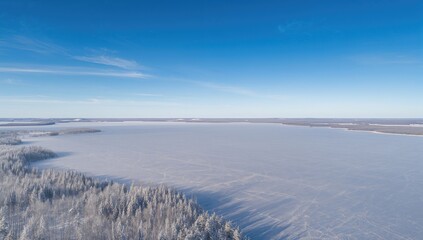 Drone shot capturing an icy lake extending into the distance under a clear blue sky during winter.
