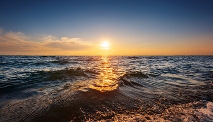 Obraz premium The Sun Descends Towards The Horizon Casting A Warm Glow On The Ocean Surface As Gentle Waves Create A Sparkling Effect In The Evening Light