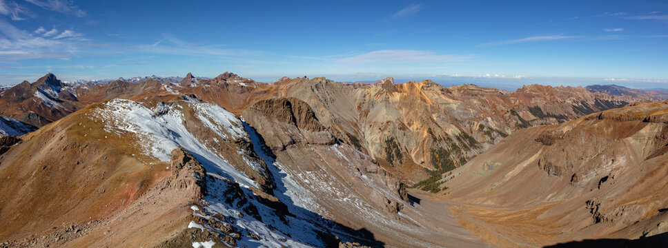 This stunning Colorado autumn mountain panorama features the Cimarrons of the northern San Juan Mountain Range, capturing their rugged volcanic pinnacles and vibrant colors under a blue sky.