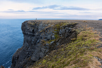 A lone figure on the clifftop looks out over the Barents Sea from North Cape, Magerøya, Northern Norway.  The single figure gives scale to the mighty cliffs and emphasises the remoteness.