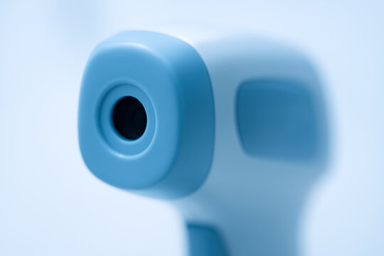 Macro photo of a modern blue-and-white infrared thermometer, highlighting its clean plastic texture and lens opening under soft lighting.