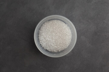Primary polystyrene granules in round plastic container, top view. Granulated plastic polymer. PS granules or EPS beads.  Virgin GPPS pellets
