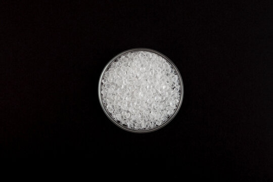 Virgin polystyrene granules in Petri dish on black background, top view. Granulated plastic polymer. PS granules or EPS beads. Virgin GPPS pellets