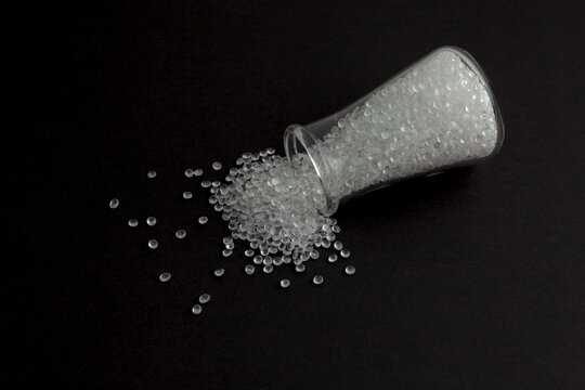 Polystyrene granules spilled out of laboratory flask on dark surface. Granulated plastic polymer. PS granules, transparent beads. Virgin GPPS pellets