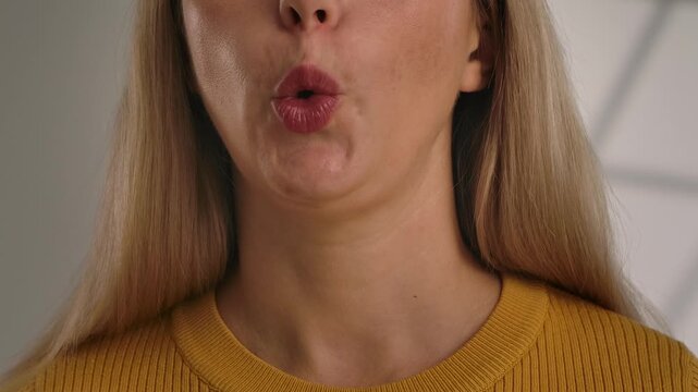 Close up of a mouth whistling. A woman mouth forming the shape of the letter O, filmed against a neutral background. Slow motion.
