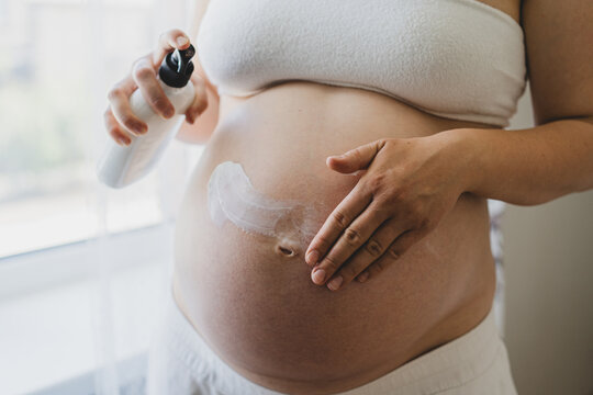 A pregnant woman applies skincare cream to her skin. This moment emphasizes self-care during pregnancy.