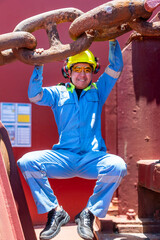 Merchant vessel officer poses under the large, rusted anchor chain on deck of container ship.