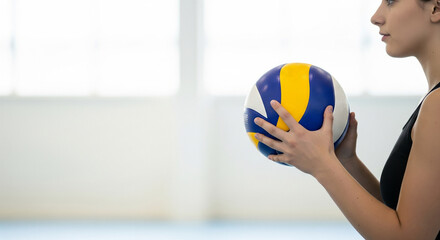 Young female athlete holds a volleyball, ready to serve or play, in a brightly lit indoor sports court