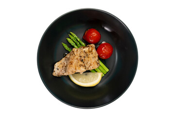 Red snapper steak, asparagus, tomatoes, and lemon on a black plate on a white background. Table top view.