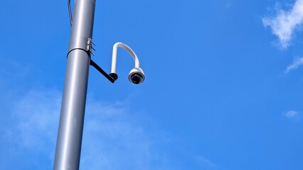 Modern white dome CCTV camera mounted on a grey pole against bright blue sky for security or public safety applications © Adrenaloby