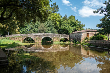 Fototapeta premium Ponte de pedra histórica e Azenha em Estorãos em Ponte de Lima com o reflexo das estruturas centenárias e da vegetação exuberante nas águas calmas do rio