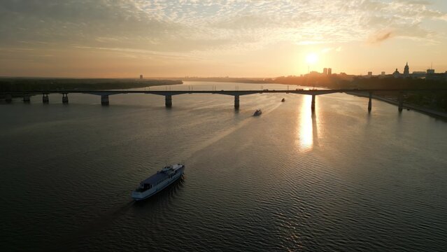 Passenger ferry crossing river at sunset near city bridge. Clip - Powered by Adobe