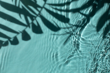 Blue water texture background on the noon sunlight with tropical leaves shadow.