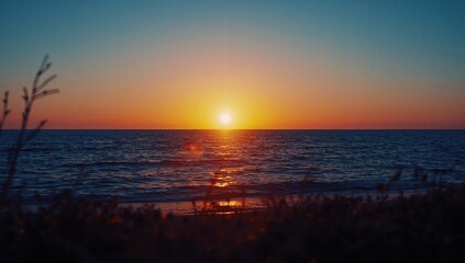Naklejka premium A tranquil dusk by the ocean paints a mesmerizing picture, with shimmering waves illuminated by the fading sunlight and soft-focus vegetation outlines in front.