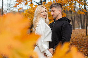 Fototapeta premium Romantic couple embracing in a park filled with golden autumn leaves, enjoying a peaceful fall day. Couple enjoying peaceful autumn vibes, wrapped in warm emotions and golden colors.